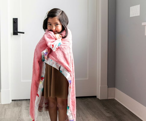 Petite fille avec une couverture rose debout devant une porte pour démontrer l'importance de l'isolation d'une porte en bois.